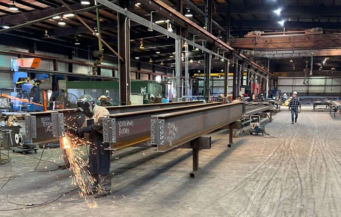 Structural steel fabrication — finishing a welded I-beam with bolted end plates in the fabrication shop