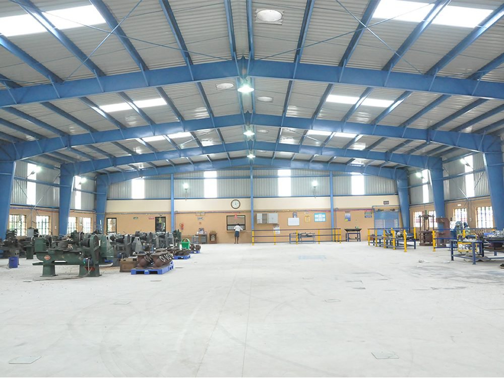Completed steel shed interior — portal frame, purlins, roof sheeting and skylight panels over a workshop floor